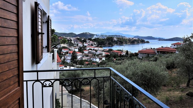 A balcony with a view of a coastal town, including houses with red roofs and a body of water. - Eye Q Resort (Skiathos)