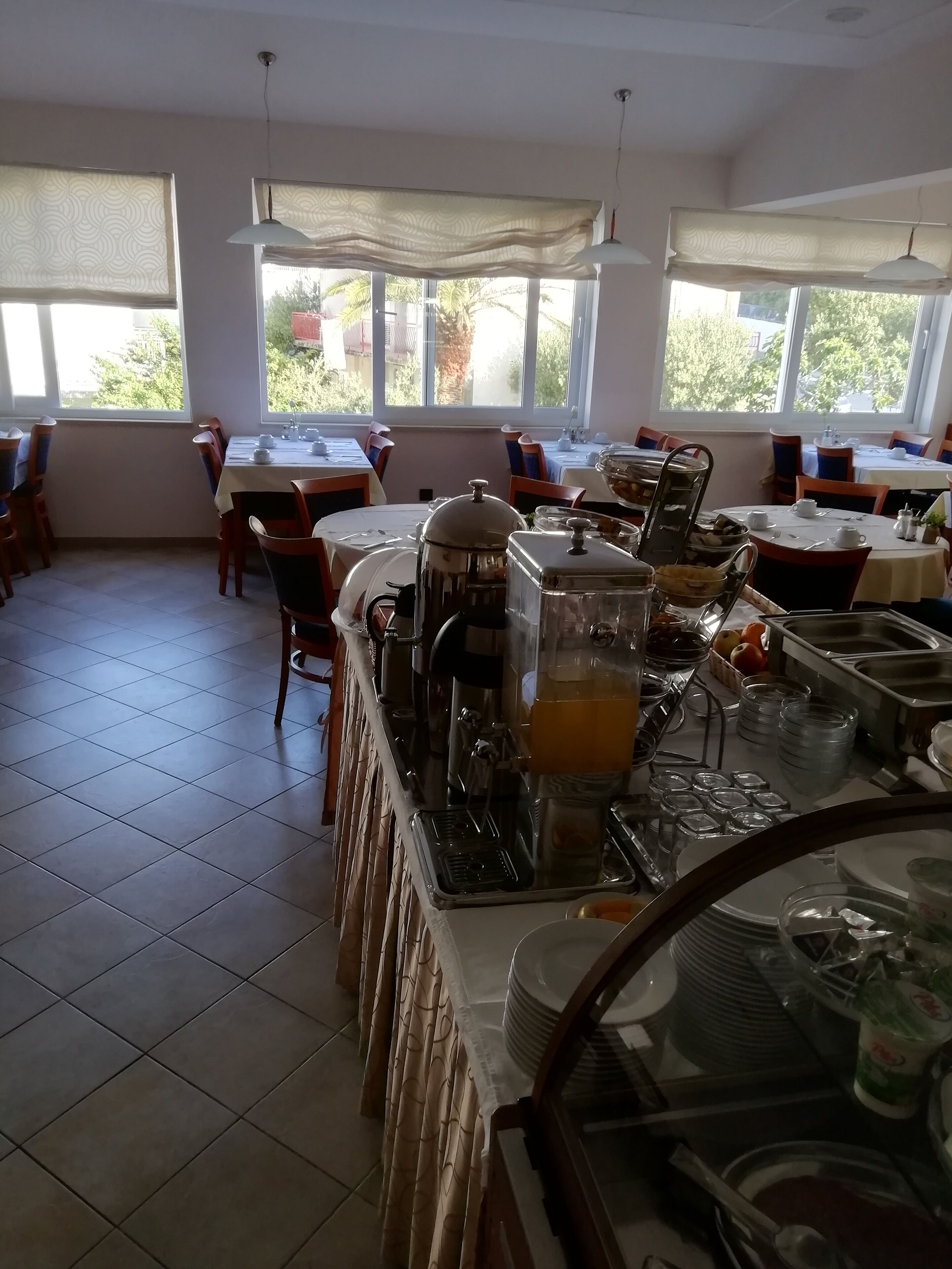 Zona de dinar amb taules preparades per a les menjades, un espai de buffet amb diversos plats i grans finestres que deixen passar llum natural.