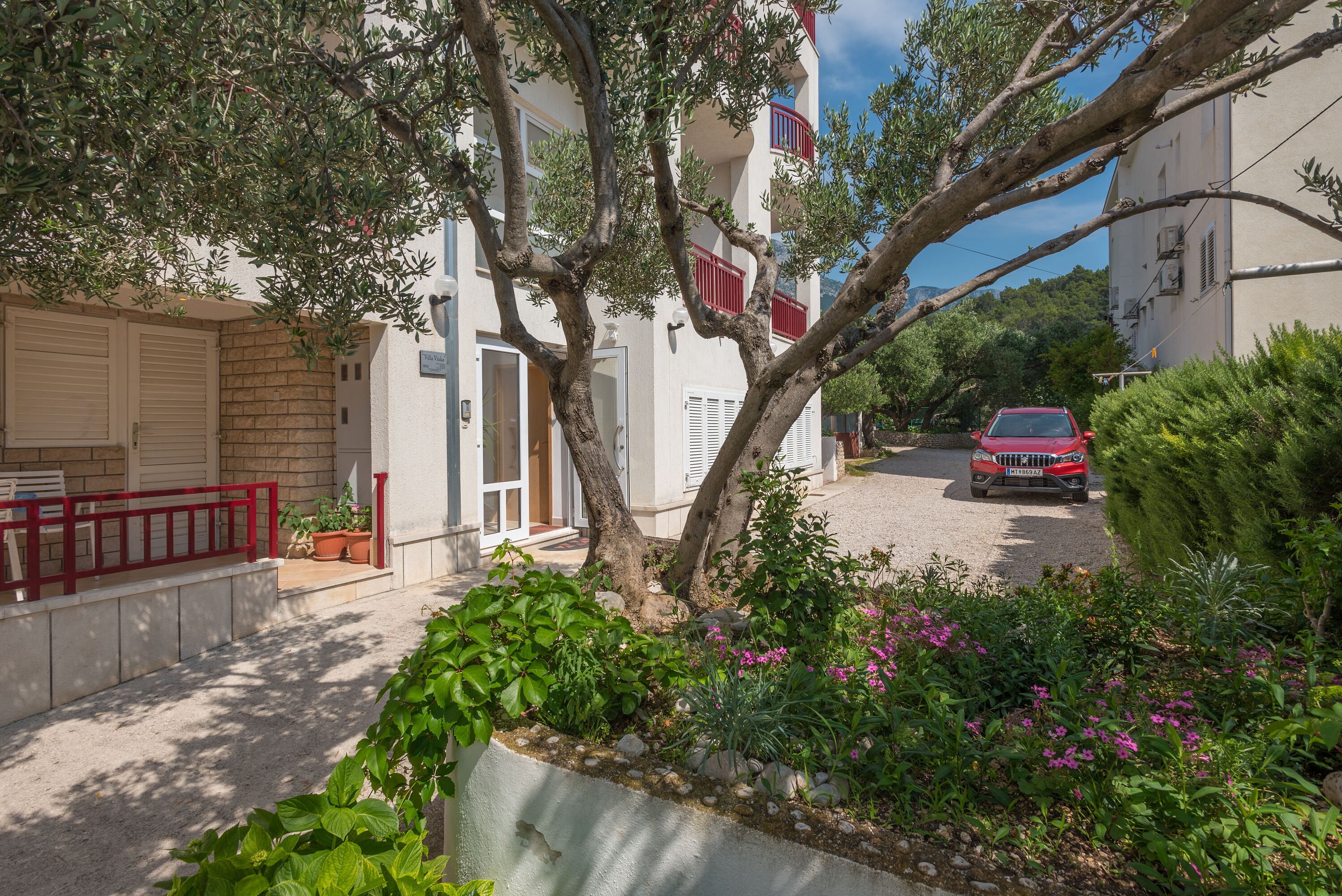 A residential building with a red car parked in front.