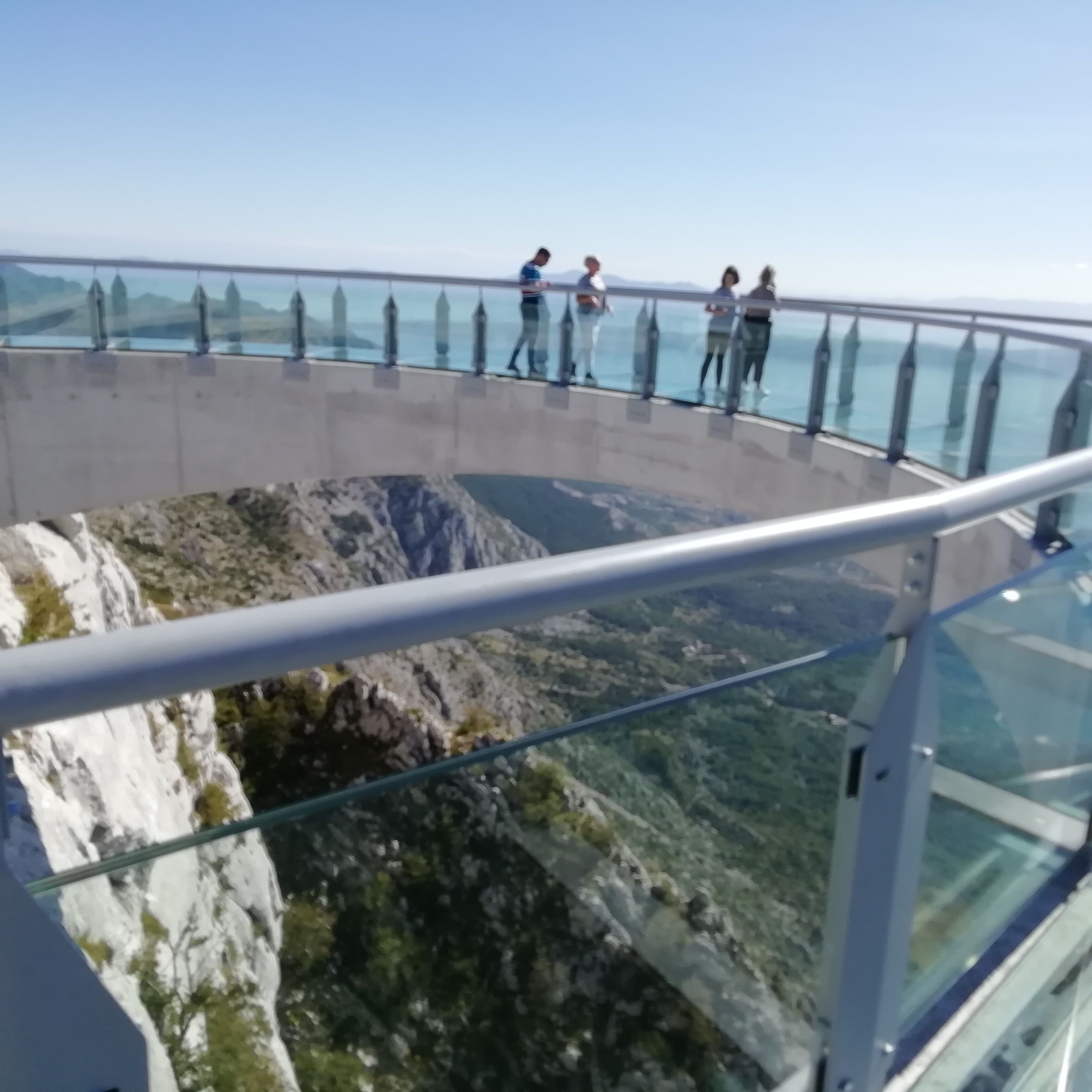 A glass observation deck with a railing overlooking a rocky landscape and a body of water.