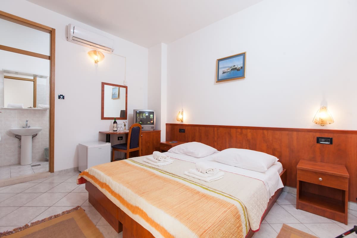 Habitación de hotel con cama, mesitas de noche, escritorio con computadora, espejo, lavamanos y un cuadro enmarcado en la pared.