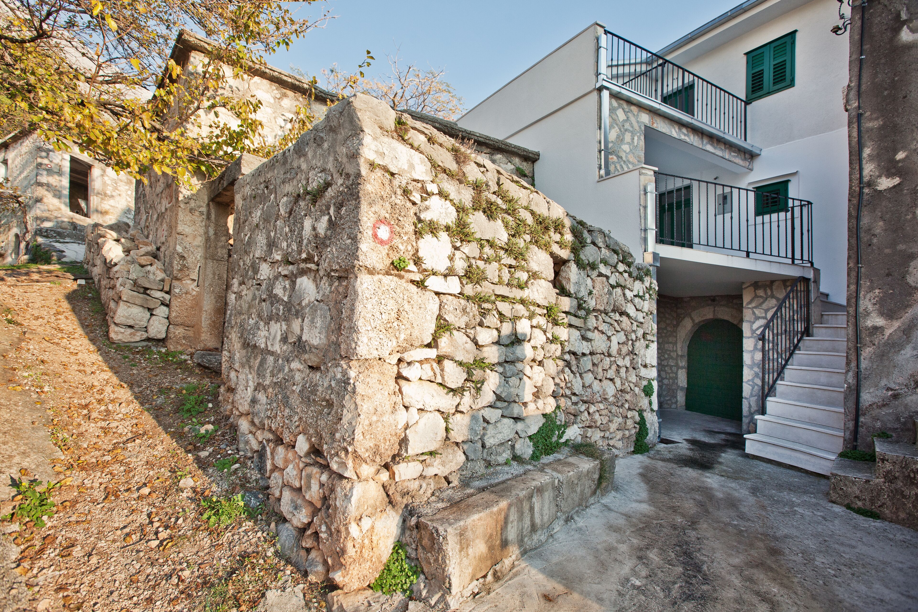 A stone wall with a staircase leading to a building with balconies.