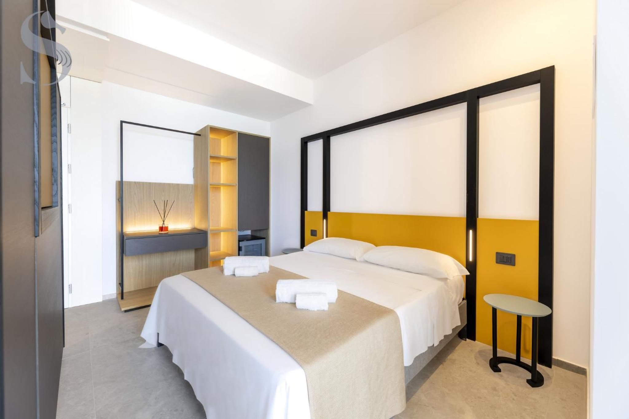 A modern hotel room with a large bed, bedside tables, a built-in shelf, and a mirror.