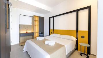 A modern hotel room with a large bed, bedside tables, a built-in shelf, and a mirror.