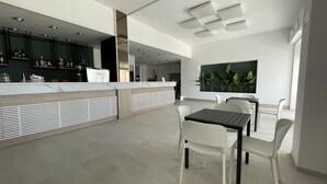 Een moderne keuken met een wit aanrecht en groene kastjes, een eethoek met een tafel en stoelen, en een groot raam met planten.