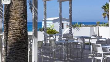 Eine Dachterrasse mit weißen Tischen und Stühlen mit Blick auf einen Strand.