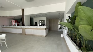 Een ruime receptie met een marmeren balie, een grote plant in pot en een modern design.