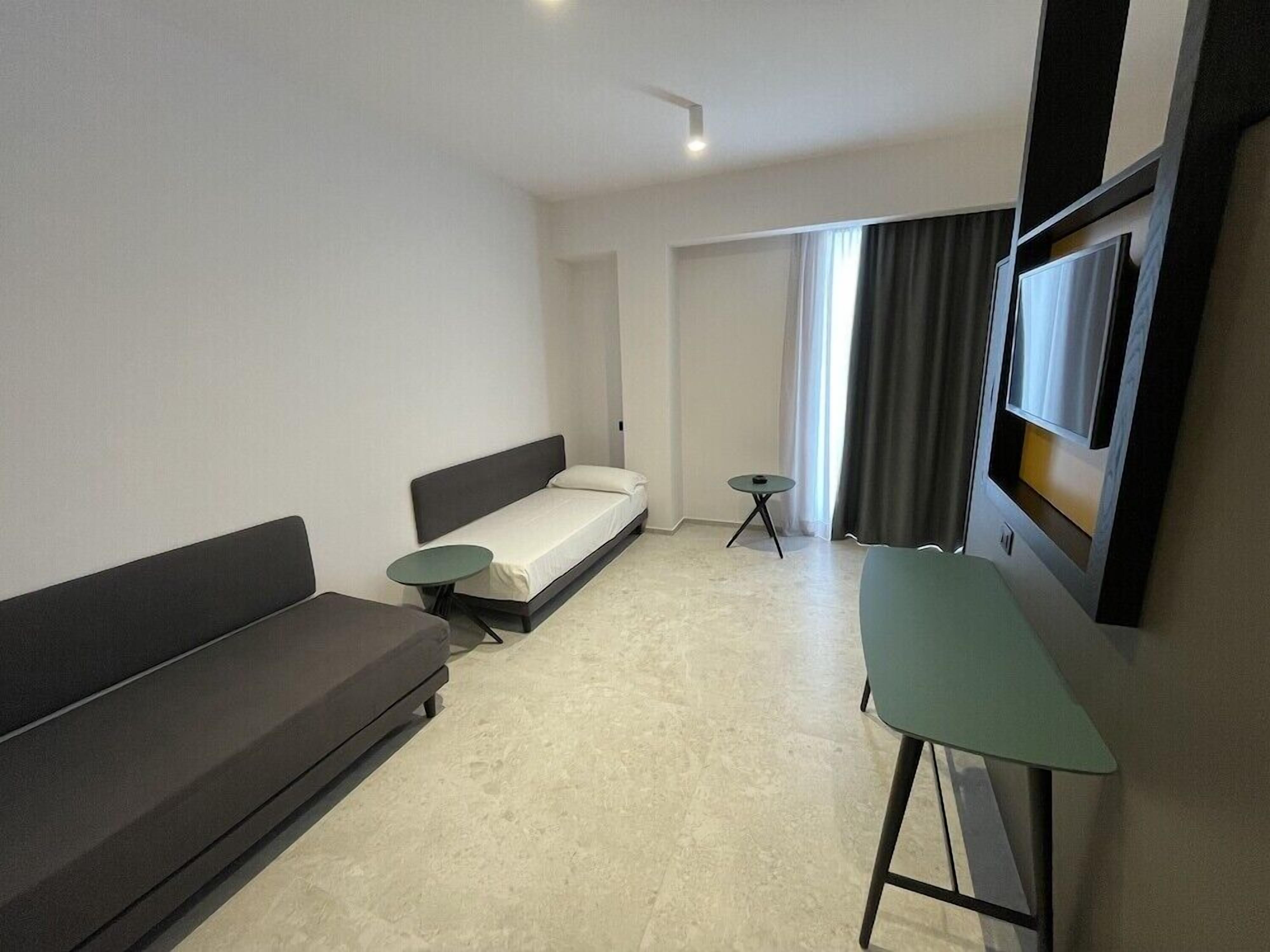 A modern, minimalist room with a sofa, a small table, a bed, and a TV mounted on the wall.