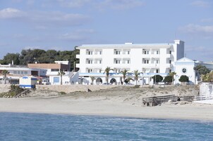Un edificio blanco de varios pisos y balcones, cerca de una playa.