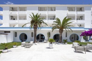 Un edificio blanco con varios balcones, palmeras y zonas de estar al aire libre.