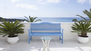 Een blauwe bank en een glazen tafel op een balkon met plantenbakken en uitzicht op zee.