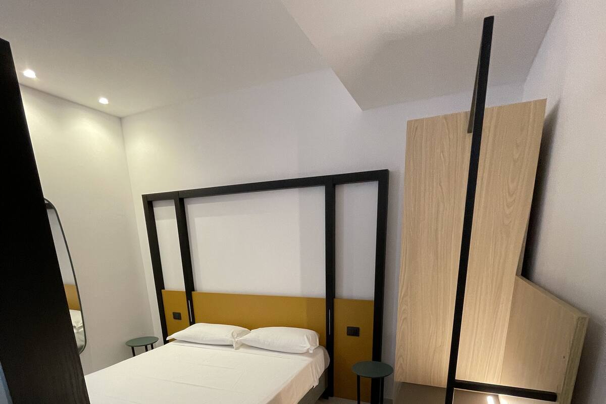 A modern hotel room with a bed, bedside tables, and a built-in bench.