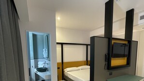 Een moderne hotelkamer met een bed, een klein tafeltje, een spiegel en een badkamer met wastafel en toilet.