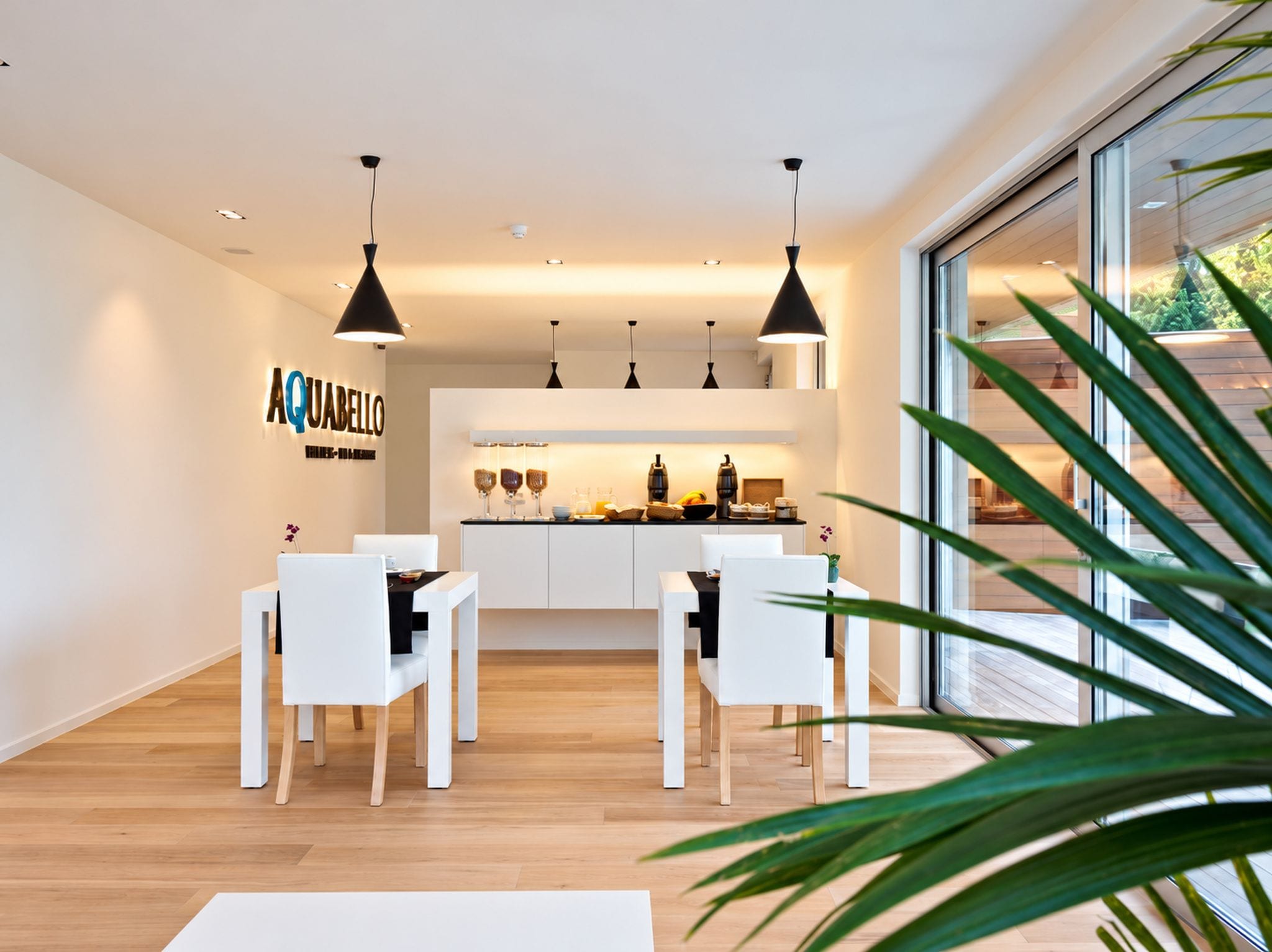 A modern kitchen with white cabinetry, pendant lighting, and a dining area with white chairs.