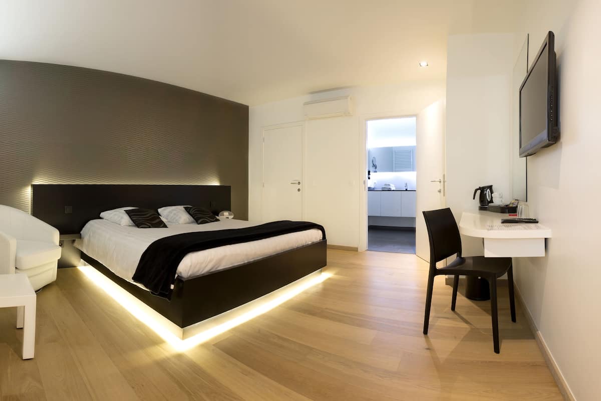 Un dormitorio moderno con cama, mesita de noche, silla, escritorio y televisor montado en la pared.