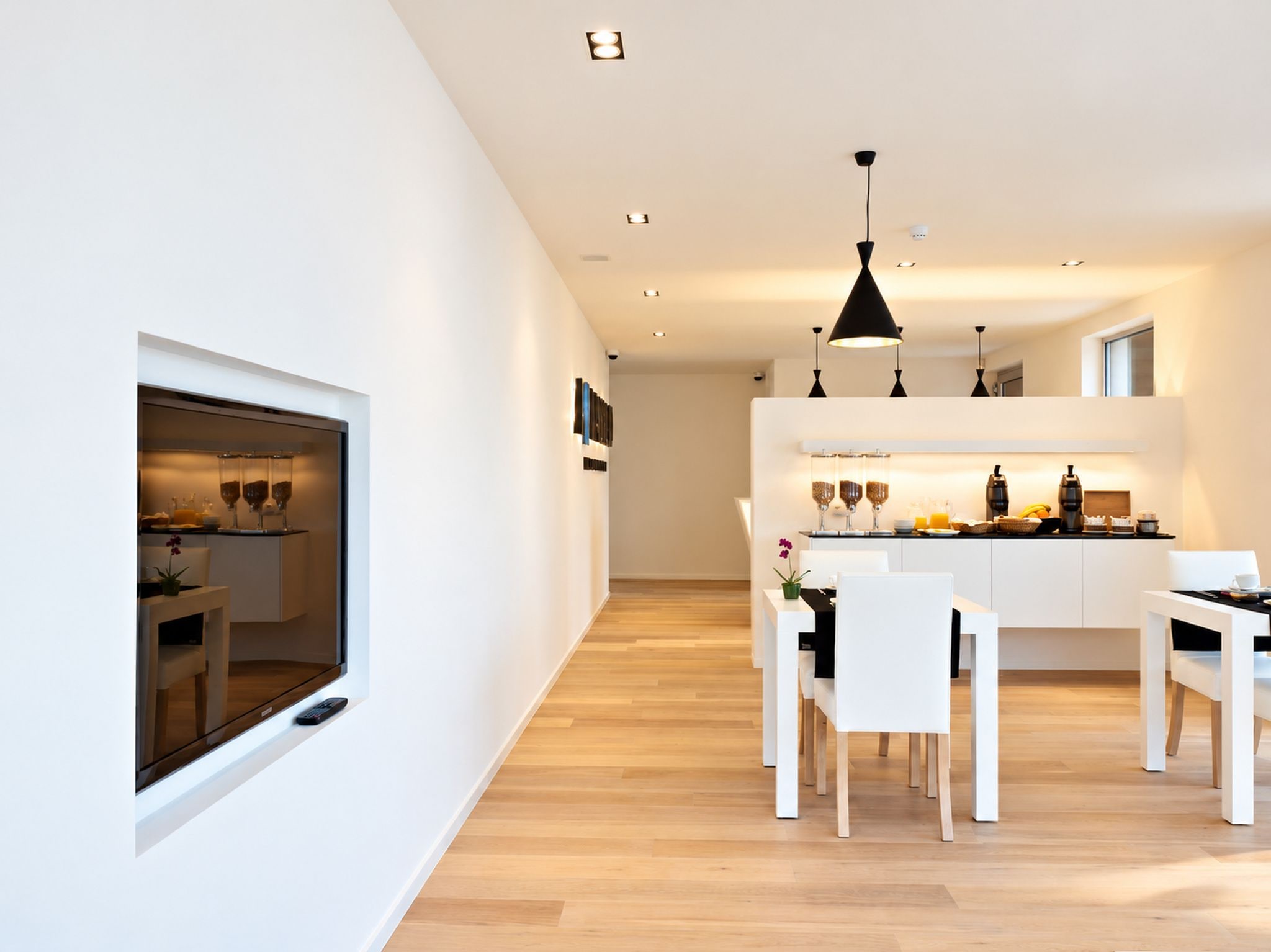 Una cocina moderna con armarios blancos, una zona de comedor con sillas blancas y un ventanal grande.