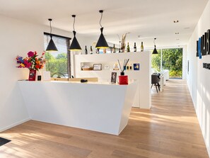 A modern reception area with a white desk, black pendant lights, and a view of greenery outside. - Aquabello (Roeselare)