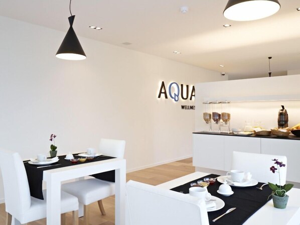 A modern dining area with white furniture, a black tablecloth, and a sign that reads "AQUA WELLNESS". - Aquabello (Roeselare)