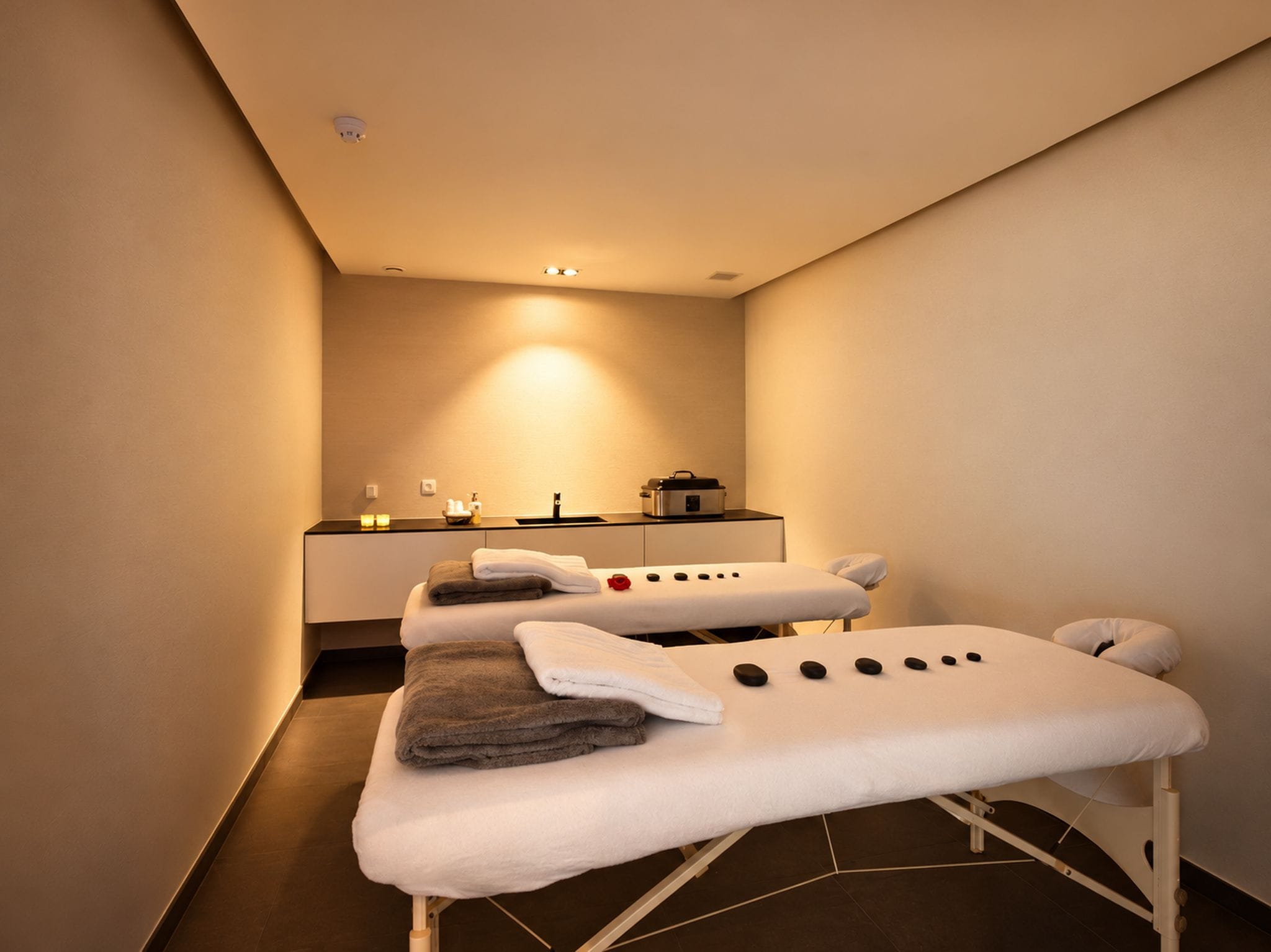 Une salle de spa équipée de deux tables de massage, de serviettes, d’un lavabo et d’une cuisinière.