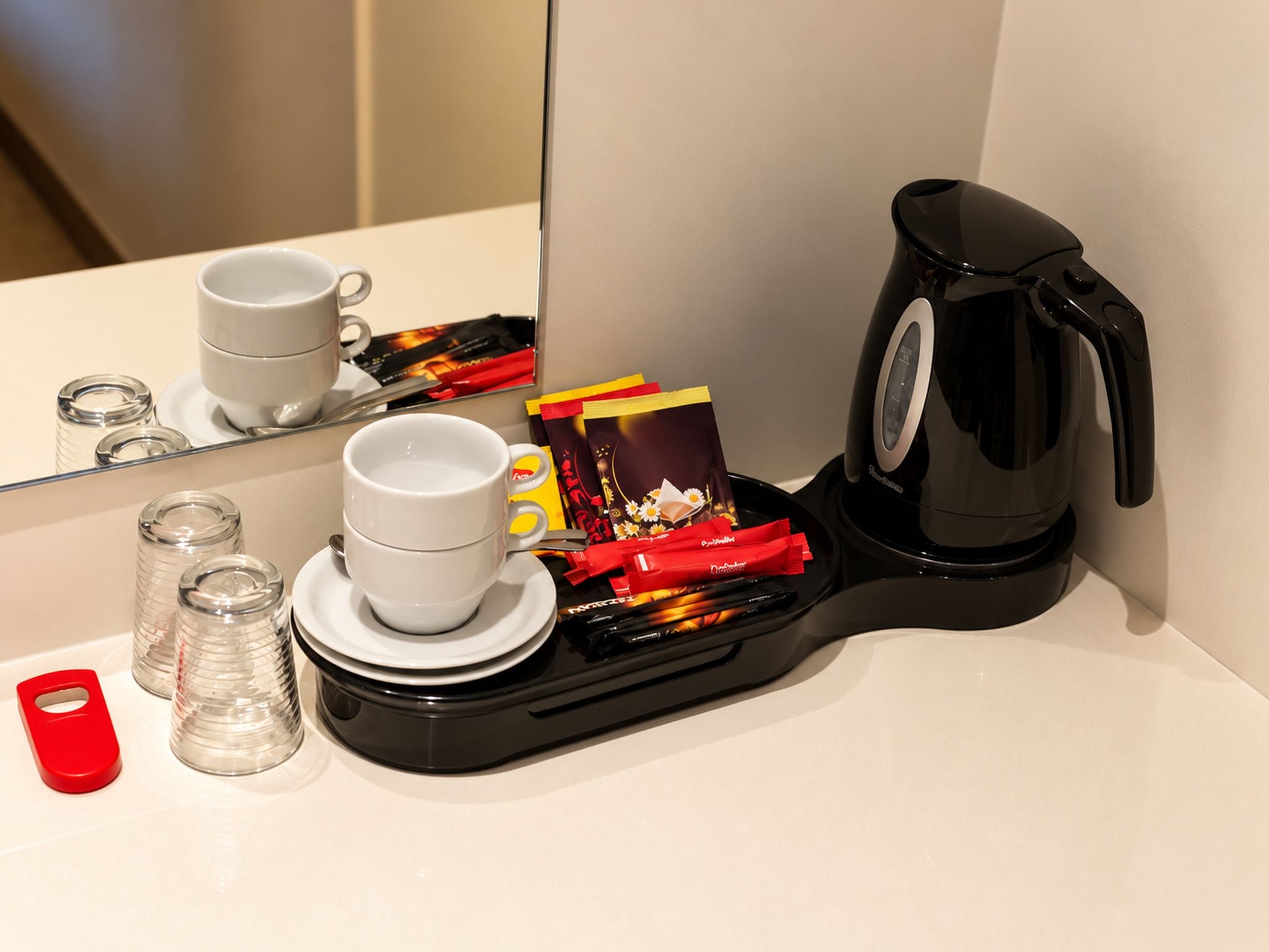 A hotel room with a coffee maker, cups, a tray with snacks, and salt and pepper shakers.