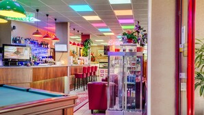 Une table de billard, un coin bar avec des chaises rouges et une vitrine.