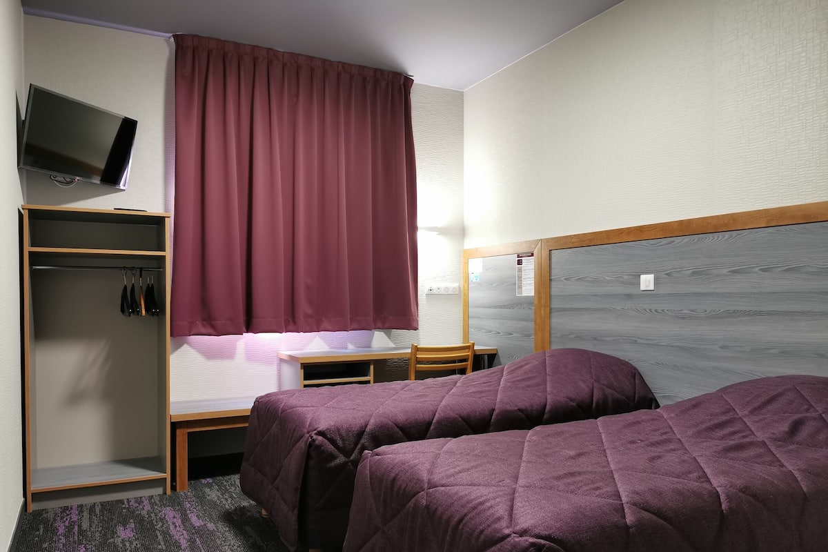 A bedroom with two beds, a TV on the wall, a wardrobe, and a desk.