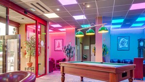 Une table de billard dans une pièce dotée d’un tapis à motifs, de murs rouges et d’un plafond équipé de luminaires disposés en réseau.