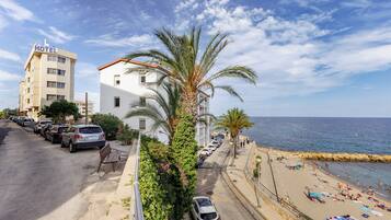 Un hôtel avec une enseigne « HÔTEL » bien visible, une plage où l’on peut prendre des bains de soleil, et une vue dégagée sur la mer.
