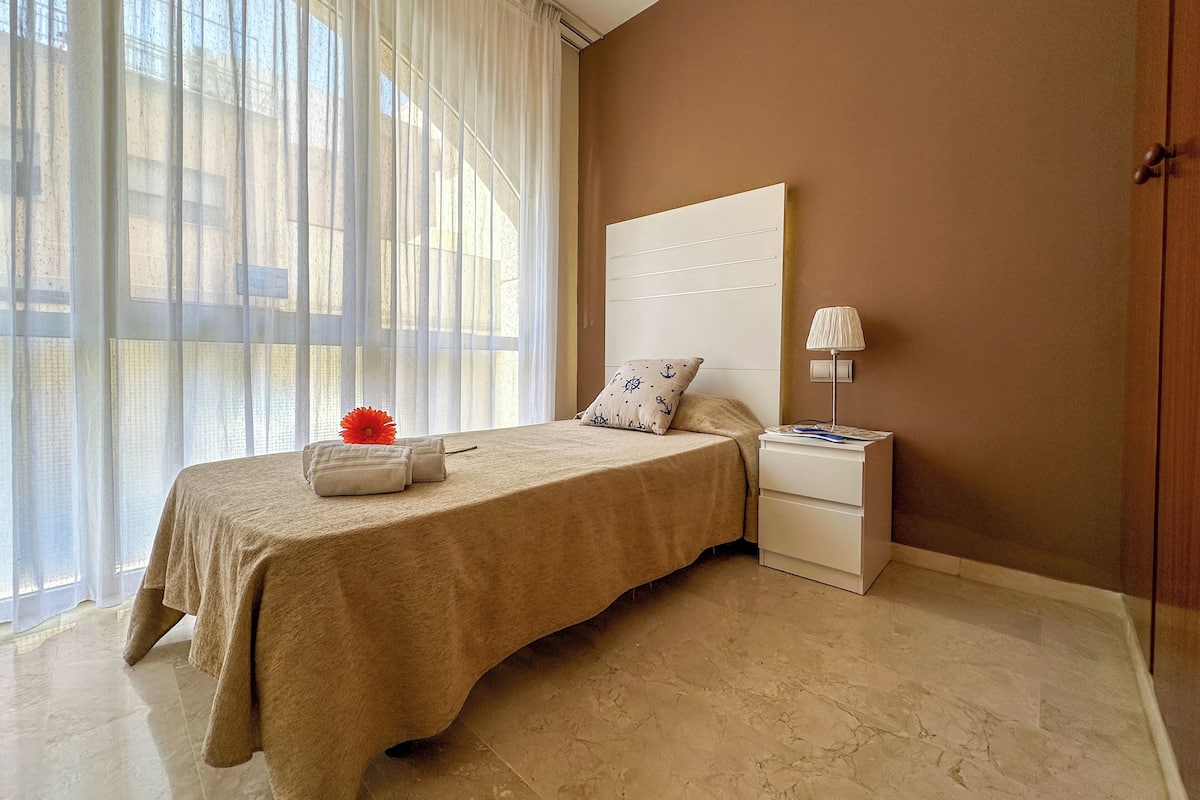 Une chambre à coucher avec un lit, une table de chevet, une lampe et des rideaux.