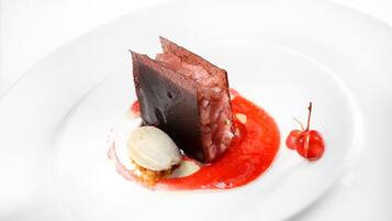 Un postre con un trozo de chocolate negro, una bola de helado y una cereza sobre un plato blanco.