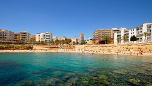 Une zone côtière caractérisée par une eau turquoise et limpide, une plage de sable et des bâtiments qui bordent le rivage.
