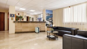 Un hall d’hôtel avec un comptoir d’accueil, un canapé en cuir noir, une petite table basse et une grande fenêtre avec des rideaux.