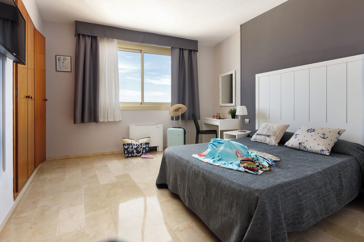 Une chambre à coucher comprenant un lit, un bureau, une chaise, une armoire, une fenêtre avec des rideaux et un radiateur.