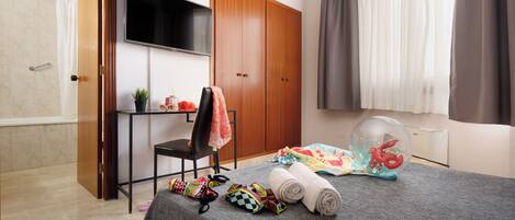 Habitación de hotel con cama, televisión, armario, silla y zona de ducha.