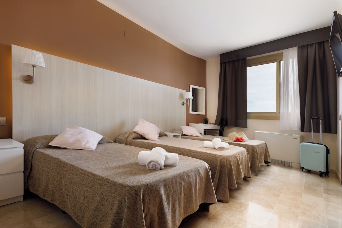 Une chambre d’hôtel avec deux lits simples, un bureau avec un ordinateur, une télévision et une fenêtre avec des rideaux.