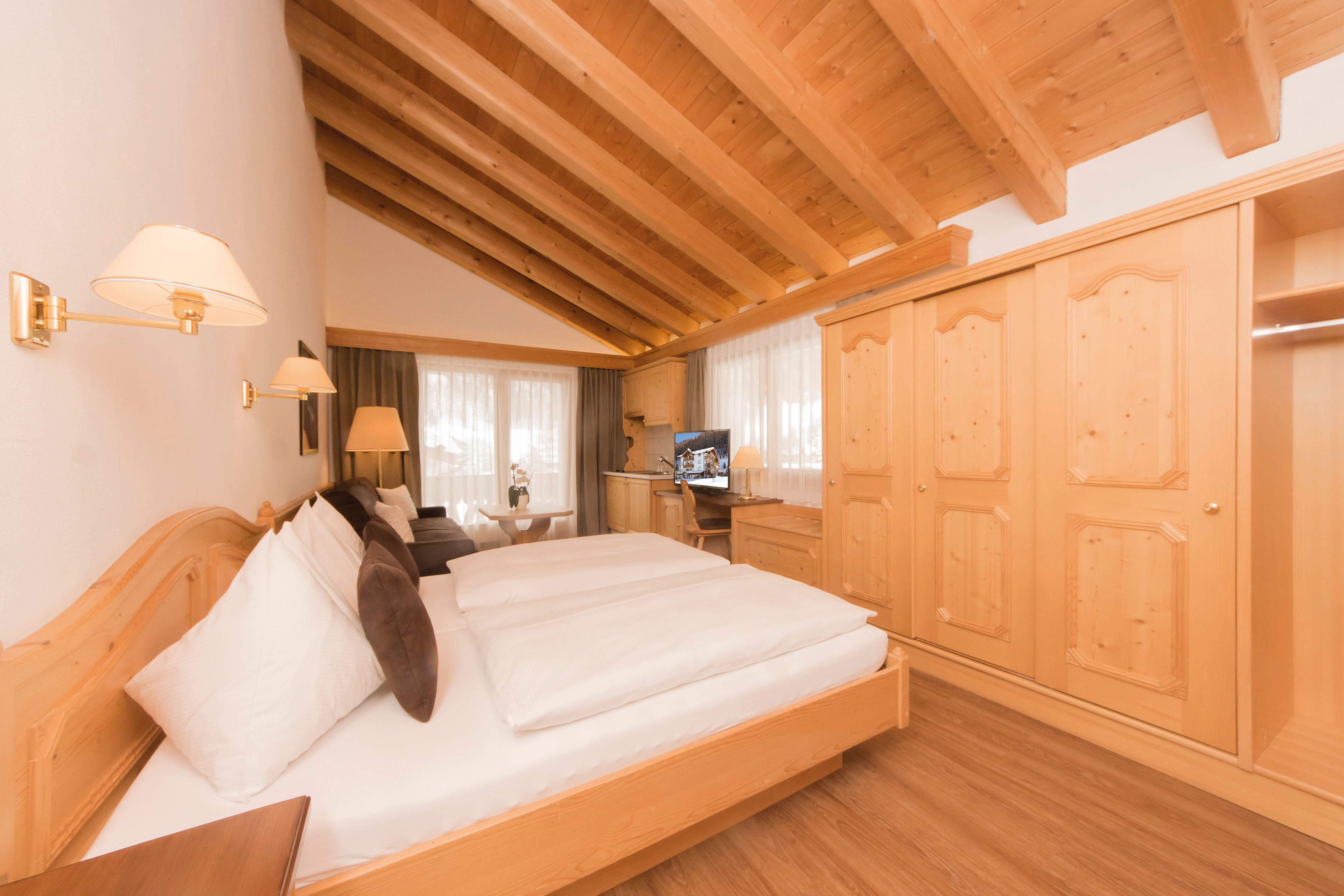 Een hotelkamer met een houten plafond, een bed met witte lakens, een televisie en een kledingkast.
