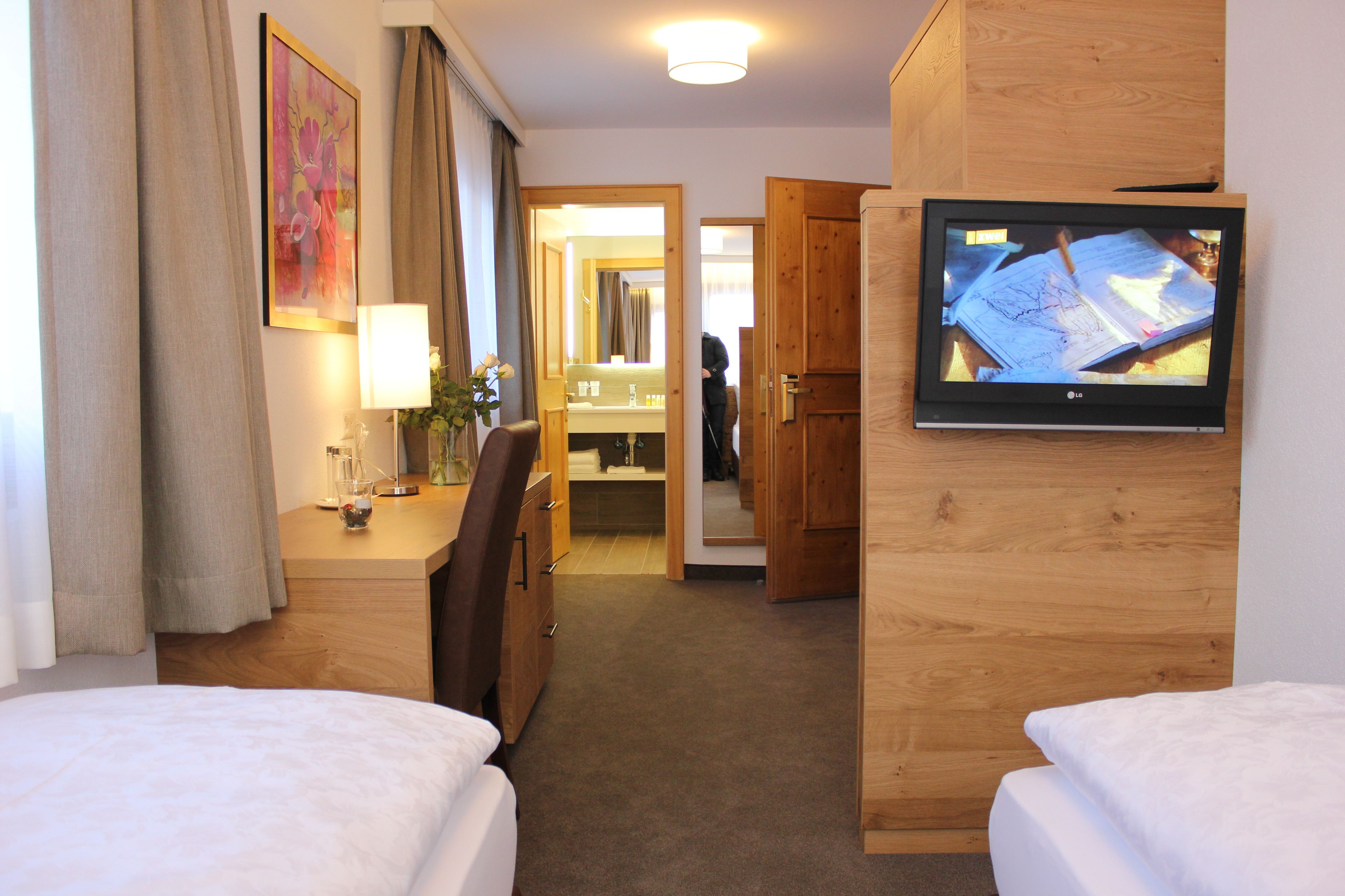 Una habitación de hotel con cama, escritorio, silla, televisor y espejo.