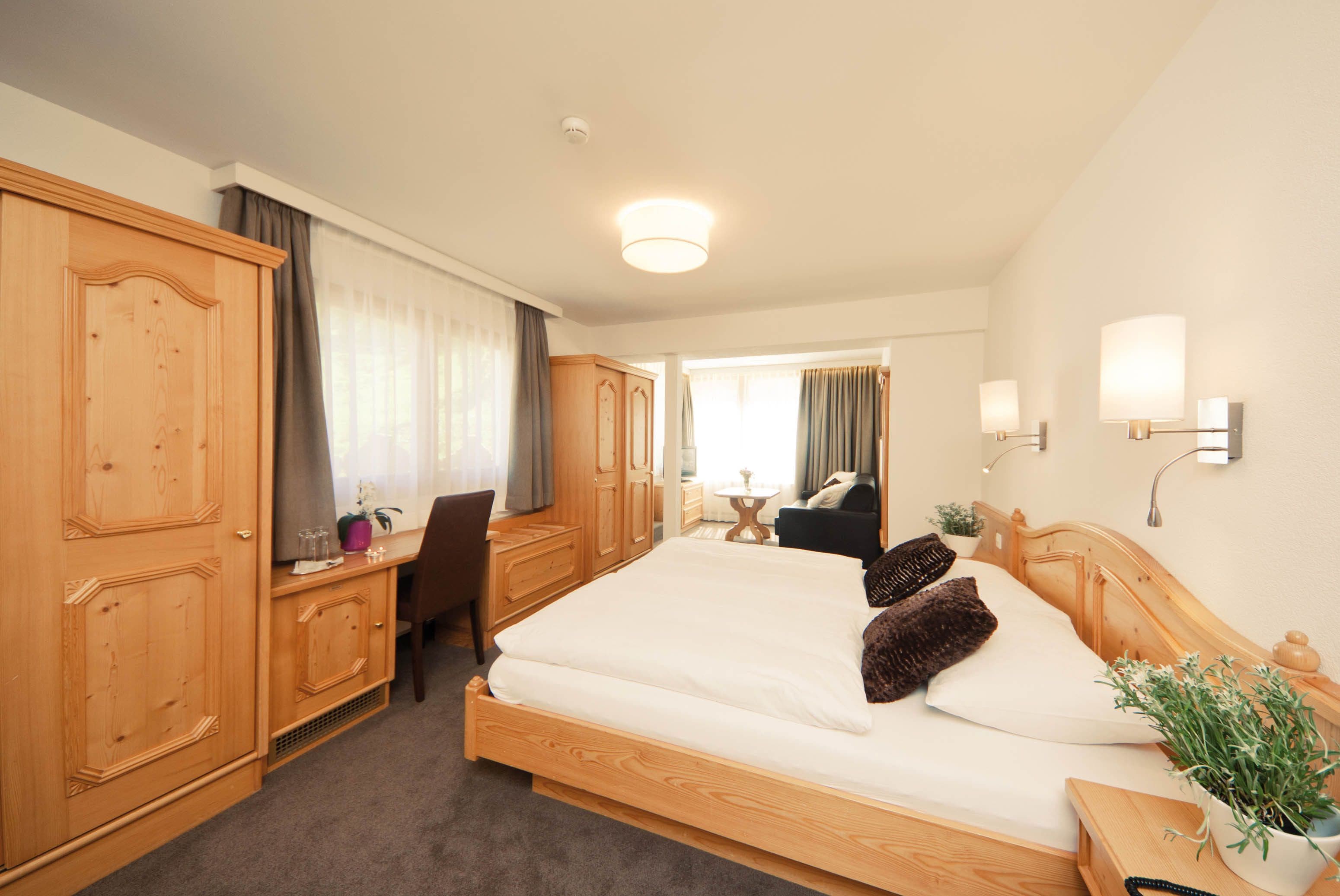 A hotel room with a large bed, wooden wardrobe, desk, and chair.
