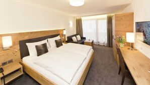 A hotel room with a large bed, a desk, a chair, a nightstand, and a TV. - Waldpark (Samnaun)