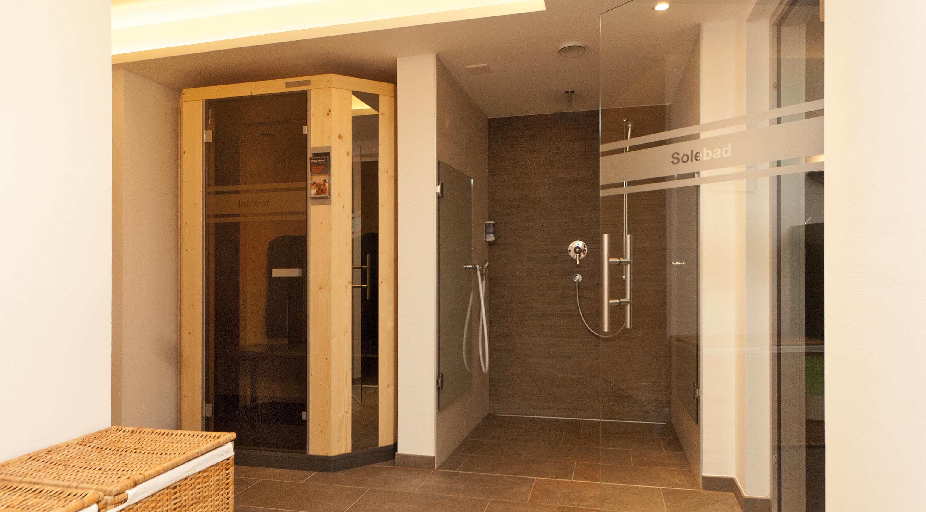 A modern bathroom with a glass shower enclosure, a visible sign reading 'Solebad,' and a wicker chair in the foreground.