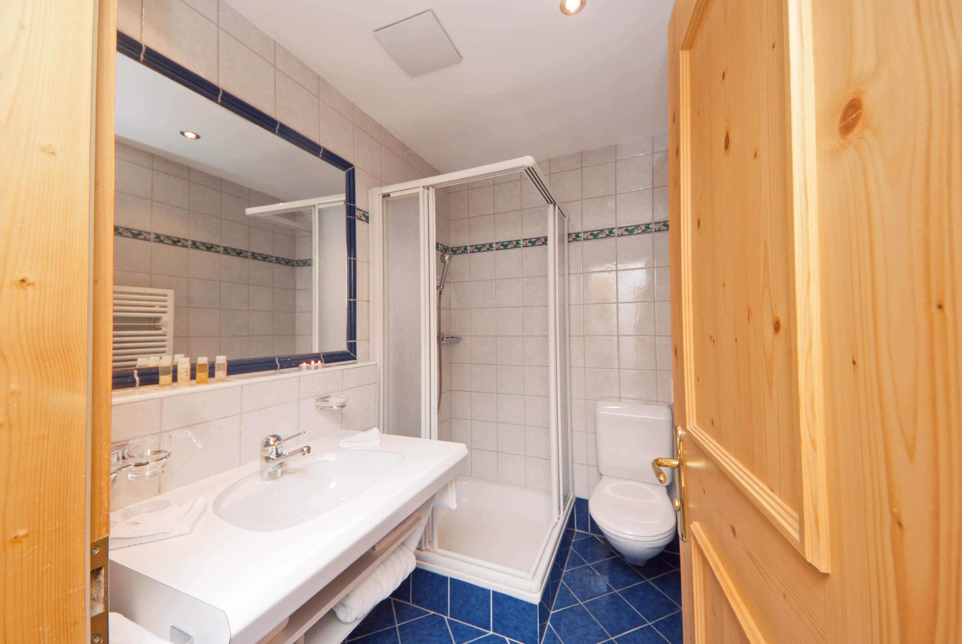 A bathroom with a shower, two sinks, a toilet, and a wooden door.