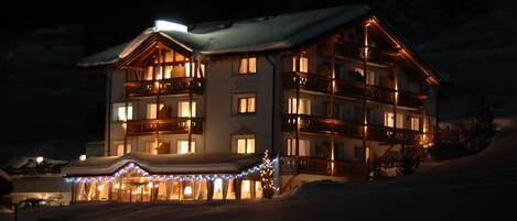 A multi-story hotel with a snow-covered roof, illuminated balconies, and a sign reading 'WALDPARK'.