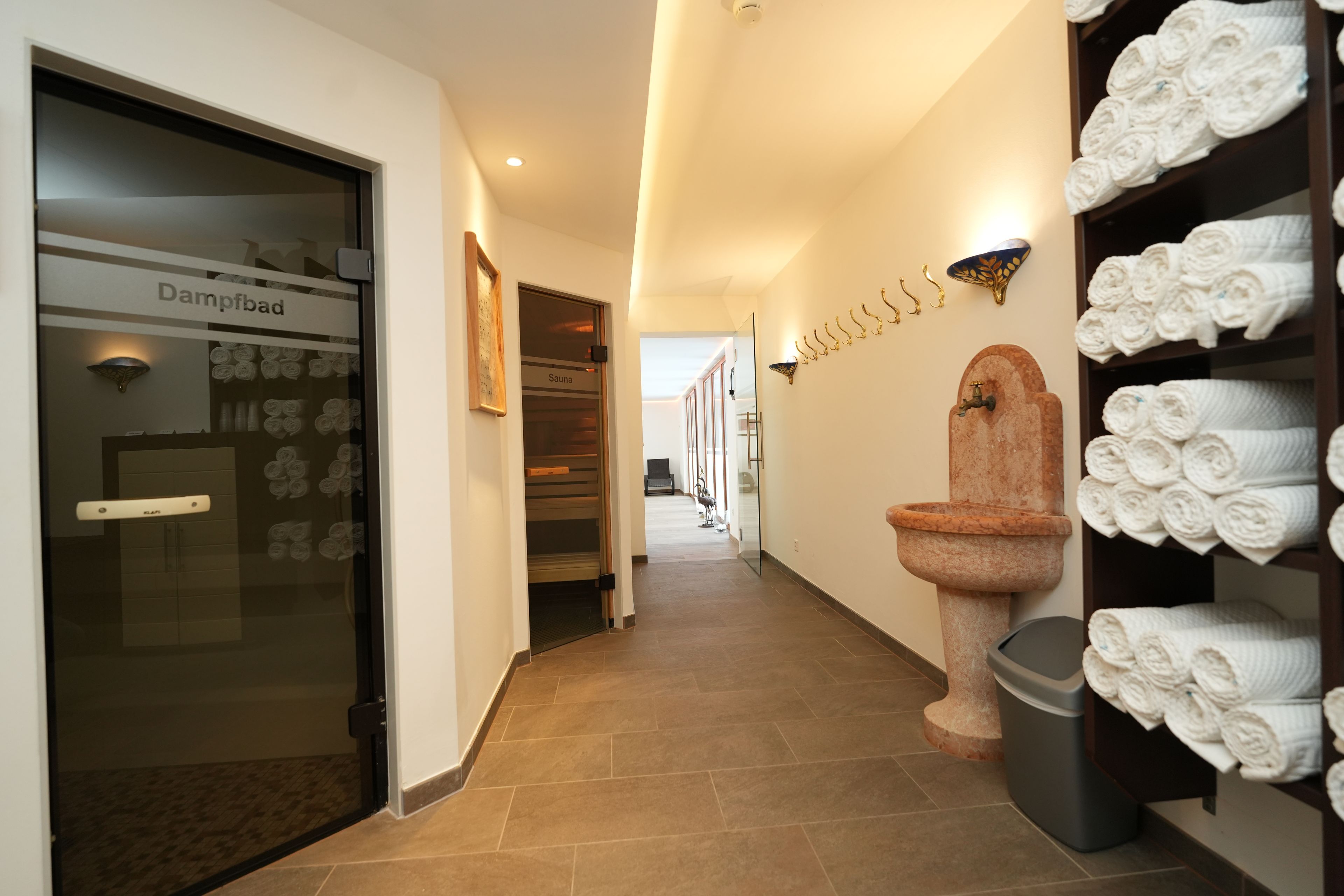 Un couloir d’hôtel avec un panneau indiquant la présence d’un sauna, un porte-serviettes et des toilettes équipées de serviettes.