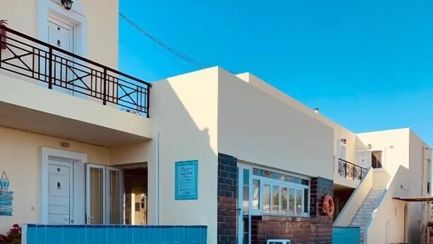 A swimming pool with a clear blue water surface, a white building with a balcony, and a lifebuoy hanging on the wall. - Manine Apartments (Kos)