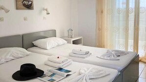A hotel room with two beds, a painting on the wall, and a window with curtains. - Manine Apartments (Kos)