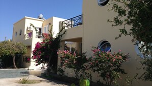 A building with multiple balconies, a garden with pink flowers, and a clear blue sky. - Manine Apartments (Kos)