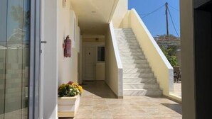 A modern building entrance with a glass door, a staircase, and a small flower arrangement. - Manine Apartments (Kos)
