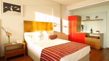 Hotelkamer met een groot bed, een nachtkastje met een telefoon en een bloevas, een rode garderobe en een klein plankje met een fles en een schaal.