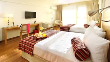 A hotel room with a large bed, a desk, a chair, a TV, and a window with curtains.