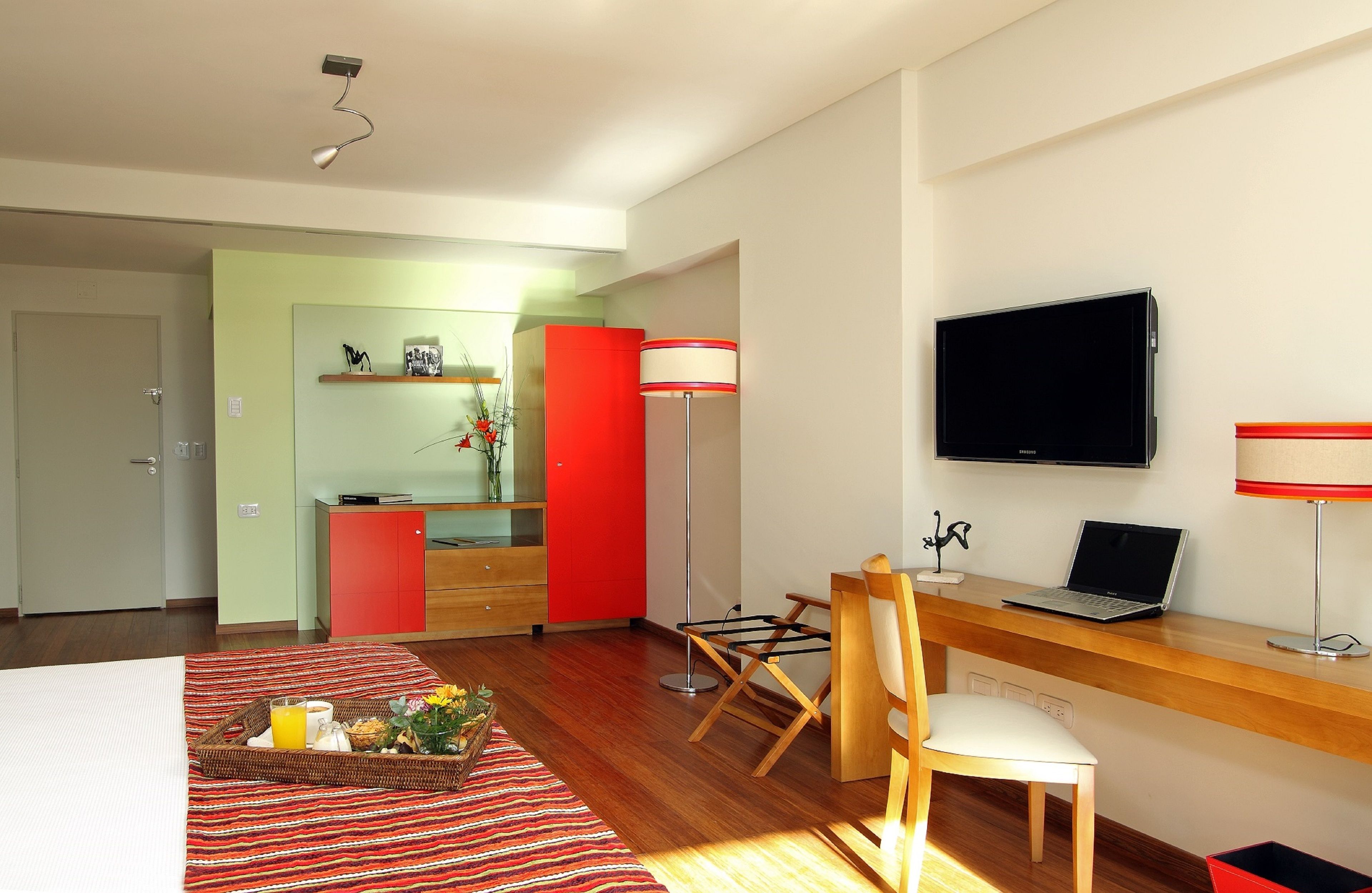 A hotel room with a bed, a desk with a laptop, a TV, a chair, and a breakfast tray.